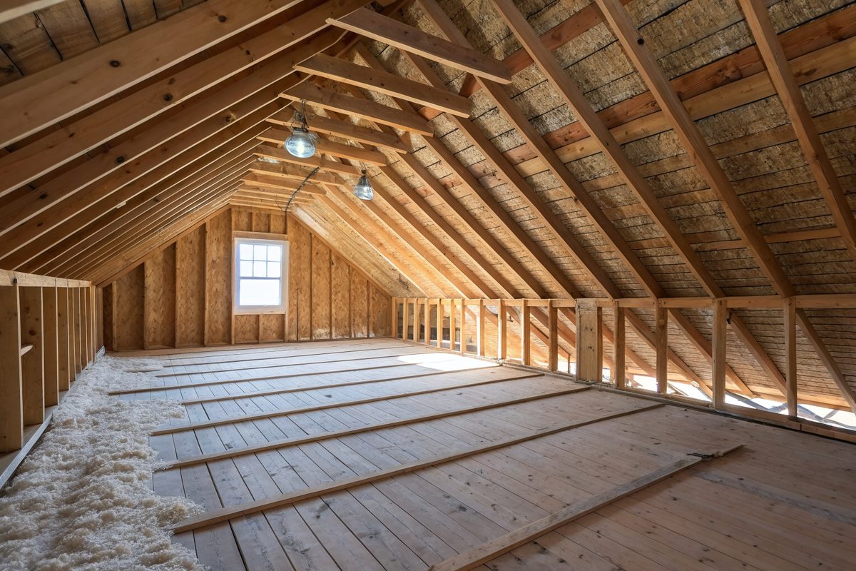 An attic with wood rafters, fresh roof decking, a small window and blown-in insulation on the floor